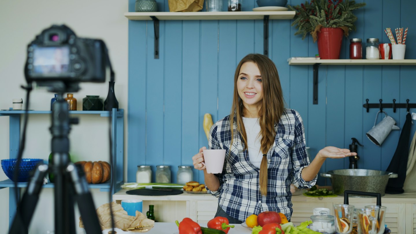 Woman recording a vlog in a modern kitchen with fresh produce.