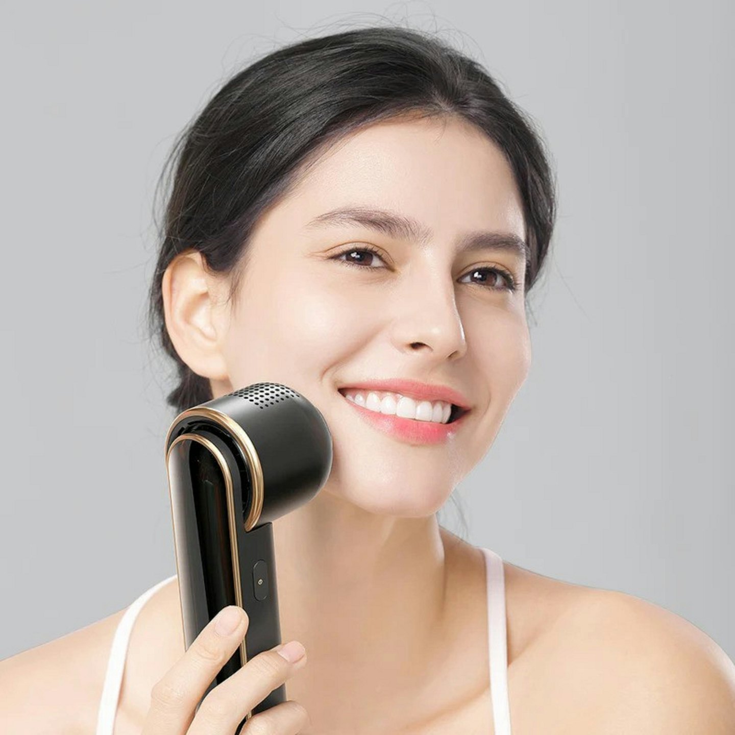 Woman smiling while holding a beauty device to her cheek.